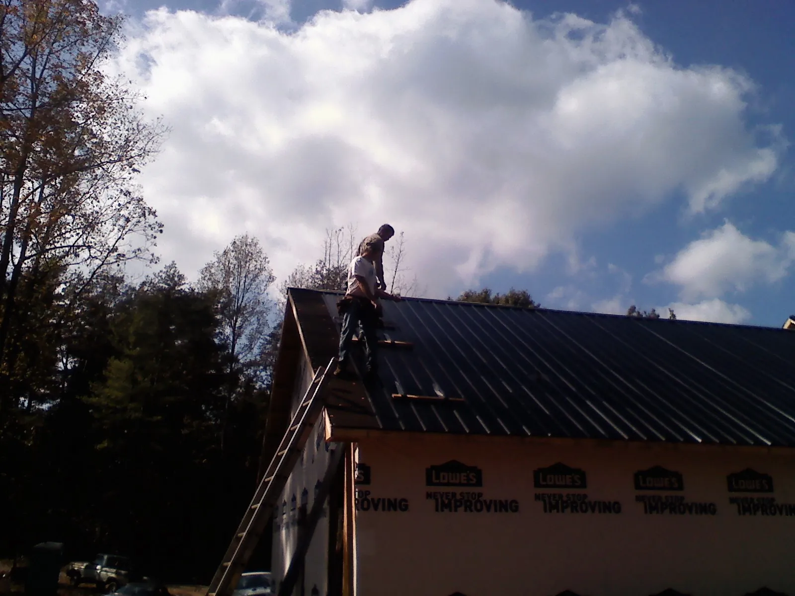 Roofer fastening dark metal panels high against a cloudy sky, from a Roof Inspection job in Somerville